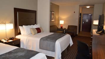 A hotel room with two beds, a desk, a chair, a TV, and a lamp.