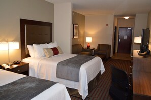 A hotel room with two beds, a desk, a chair, a TV, and a lamp.