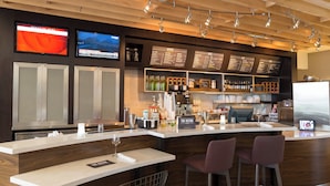 A modern bar area with a wooden ceiling, two TVs mounted on the wall, a menu board, and a bar counter with stools.