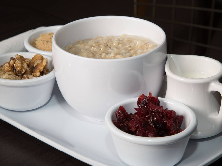 Un vassoio con una ciotola di porridge, una ciotola di noci, una ciotola di mirtilli disidratati e una piccola brocca di latte.
