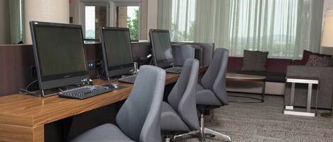 A conference room with multiple computer stations, grey office chairs, a wooden desk, and a carpeted floor.