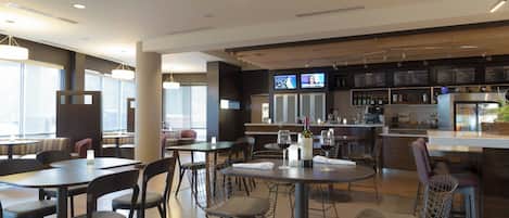 Un restaurante moderno con varias zonas de comedor, incluyendo mesas y sillas redondas, y una zona de bar con un menú a la vista.