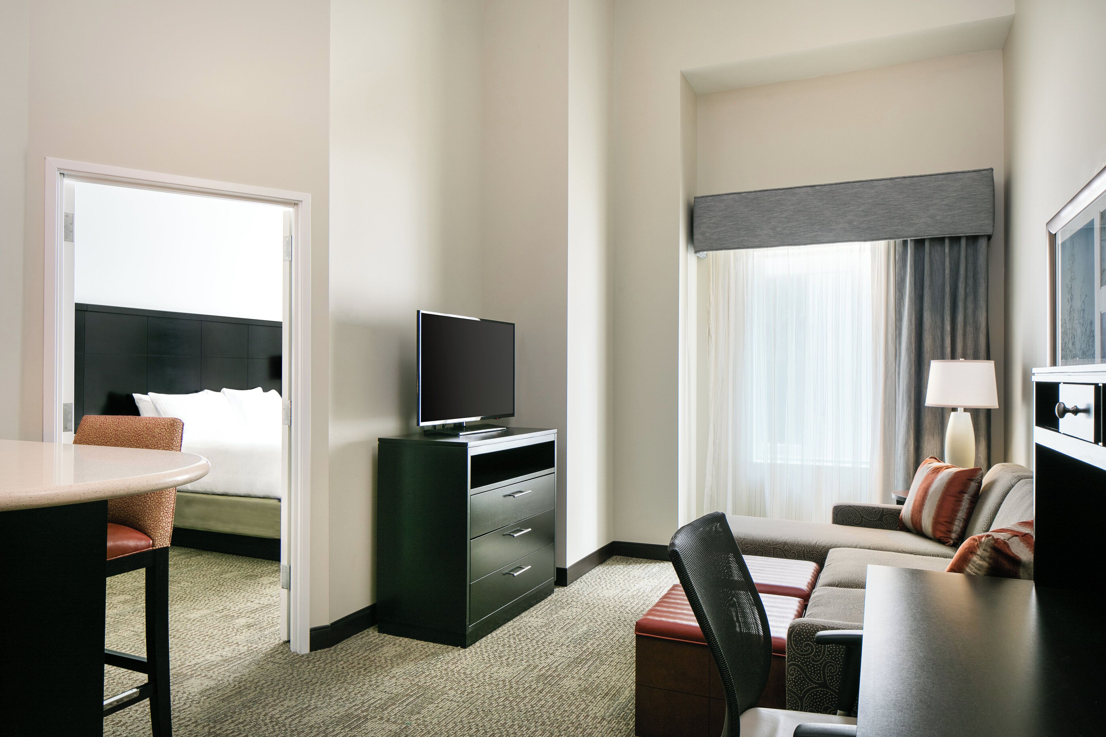 A hotel room with a bed, a desk, a television, and a window with curtains.