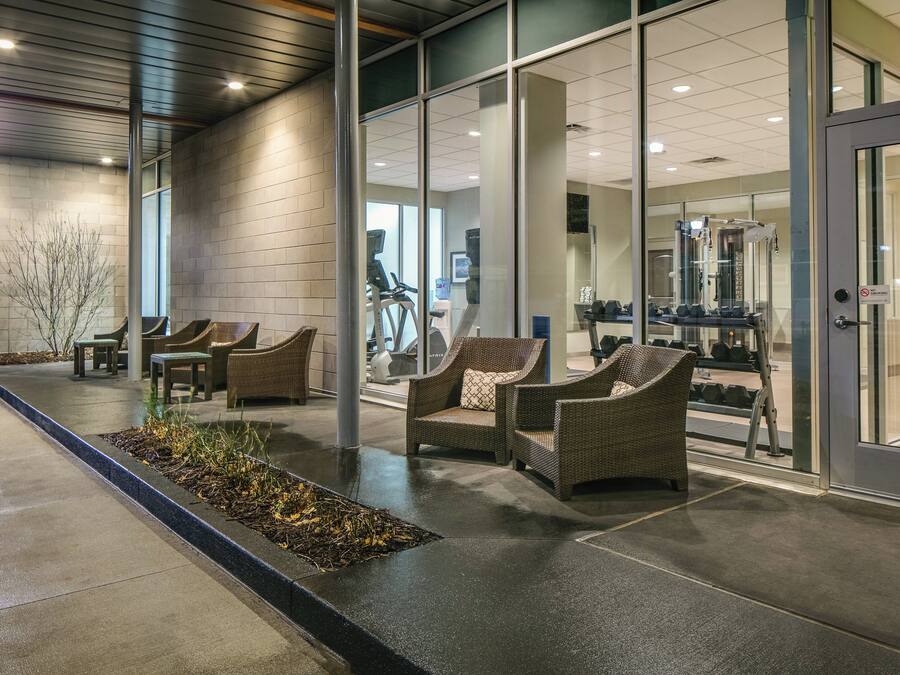 An indoor waiting area with wicker chairs, a concrete floor, and glass doors leading to a fitness area.