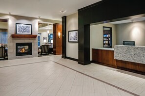 A hotel lobby with a fireplace, framed artwork, a reception desk, and a seating area. - Staybridge Suites Des Moines Downtown by IHG (Des Moines)