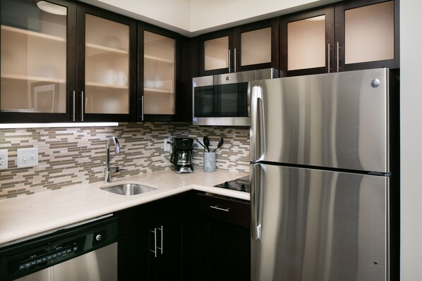A modern kitchen with dark cabinets, stainless steel appliances, and a tiled backsplash.