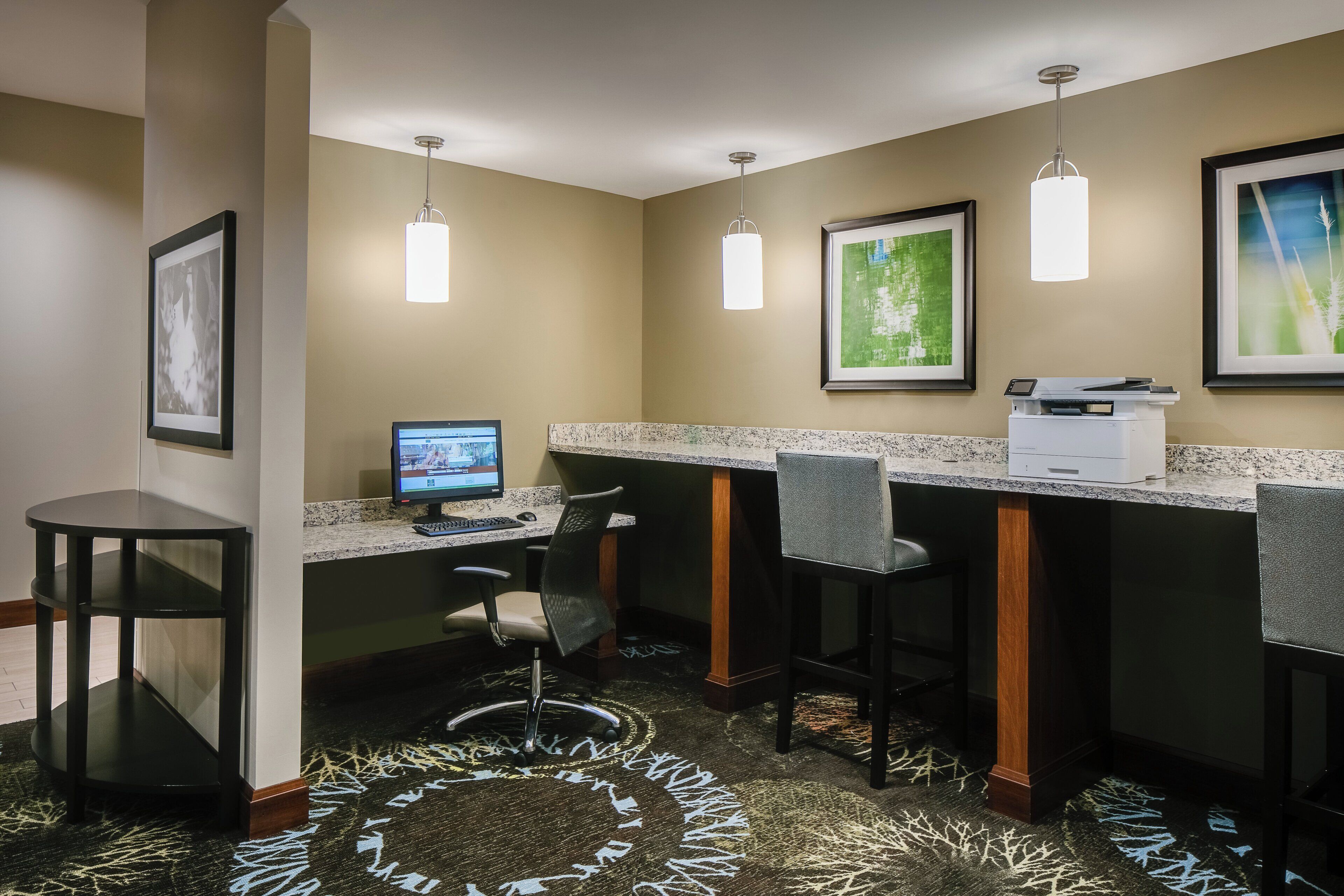 Zona de recepción de un hotel con una computadora, taburetes de bar y obras de arte enmarcadas en las paredes.