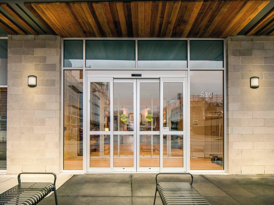 A building entrance with a glass door, two benches outside, and a wooden ceiling.