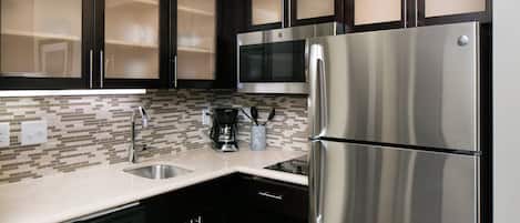 A modern kitchen with stainless steel appliances, dark cabinetry, and a tiled backsplash.