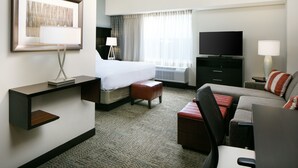 Ein Hotelzimmer mit einem Bett, einem Schreibtisch, einem Fernseher, einer Couch und einem großen Fenster mit Vorhängen.