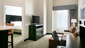 Ein Hotelzimmer mit Bett, Fernseher auf einem Schminktisch, Schreibtisch mit Stuhl, Sofa und einem Fenster mit Vorhängen.