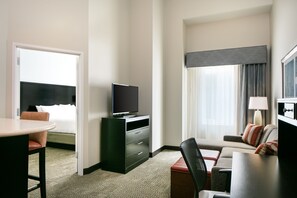 A hotel room with a bed, a TV on a dresser, a desk with a chair, a sofa, and a window with curtains.