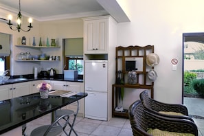 A kitchen with white cabinets, a black countertop, and a refrigerator. There is a dining table with chairs and a vase with flowers.