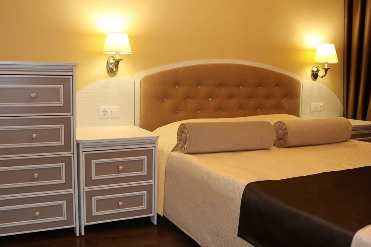 A hotel room with a large bed, two bedside tables, a dresser, and two wall-mounted lamps.