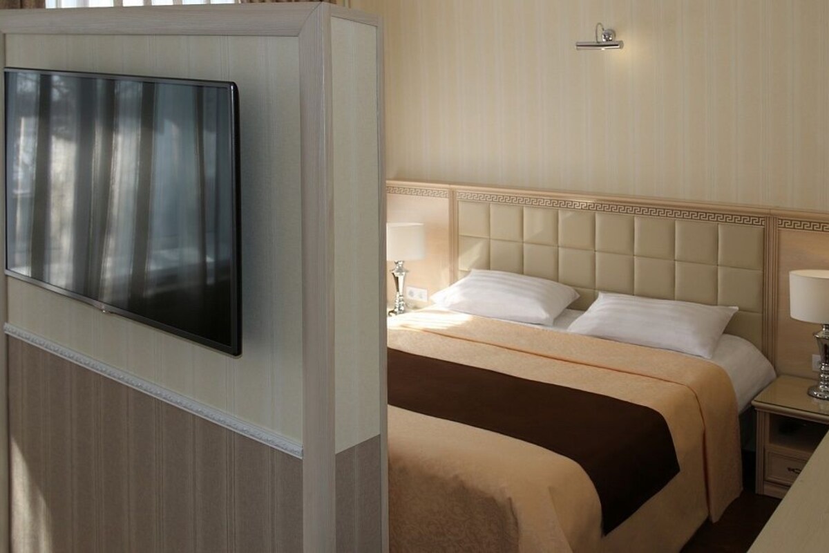 A hotel room with a large flat-screen TV mounted on the wall, a bed with a headboard featuring a geometric pattern, and bedside lamps.