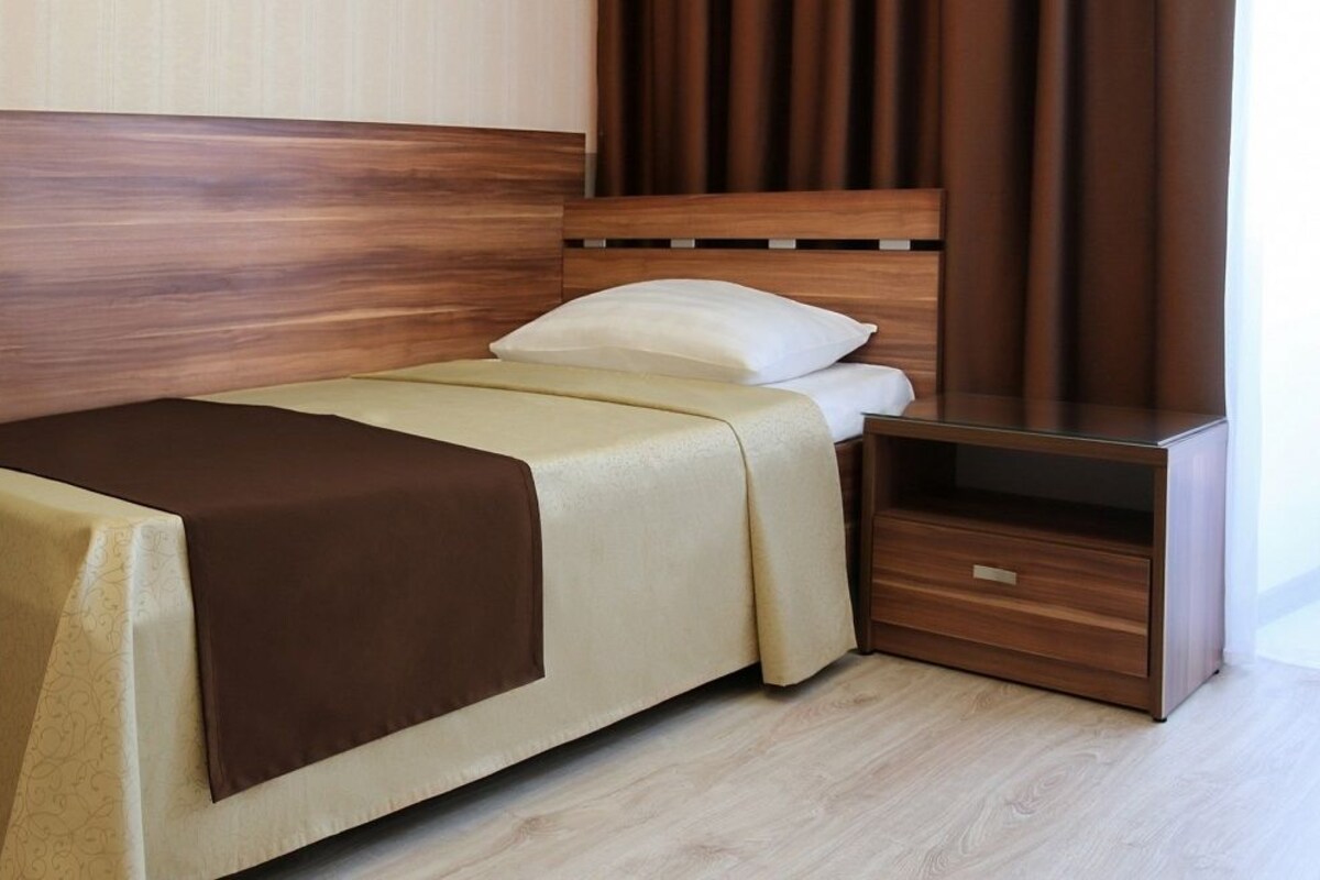 A neatly made bed with a wooden headboard, a bedside table with a drawer, and a nightstand.