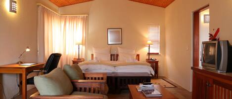 A hotel room with a wooden ceiling, a bed with white linens, a desk with a lamp, a TV on a wooden cabinet, and a chair.