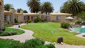 Un espacio exterior bien cuidado con césped, una piscina y edificios de piedra con marcos de ventana rojos.