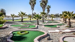 Un campo de mini golf con varios hoyos, rodeado de palmeras y una valla blanca.