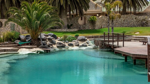 Una piscina con una cascada, rodeada de rocas y palmeras.
