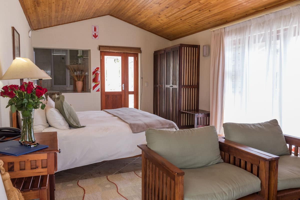Un dormitorio con una cama, una silla de madera, un escritorio con lámpara y una ventana con cortinas.