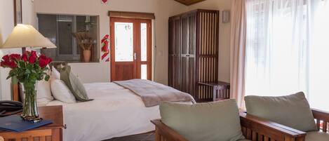A bedroom with a bed, a wooden chair, a desk with a lamp, and a window with curtains.