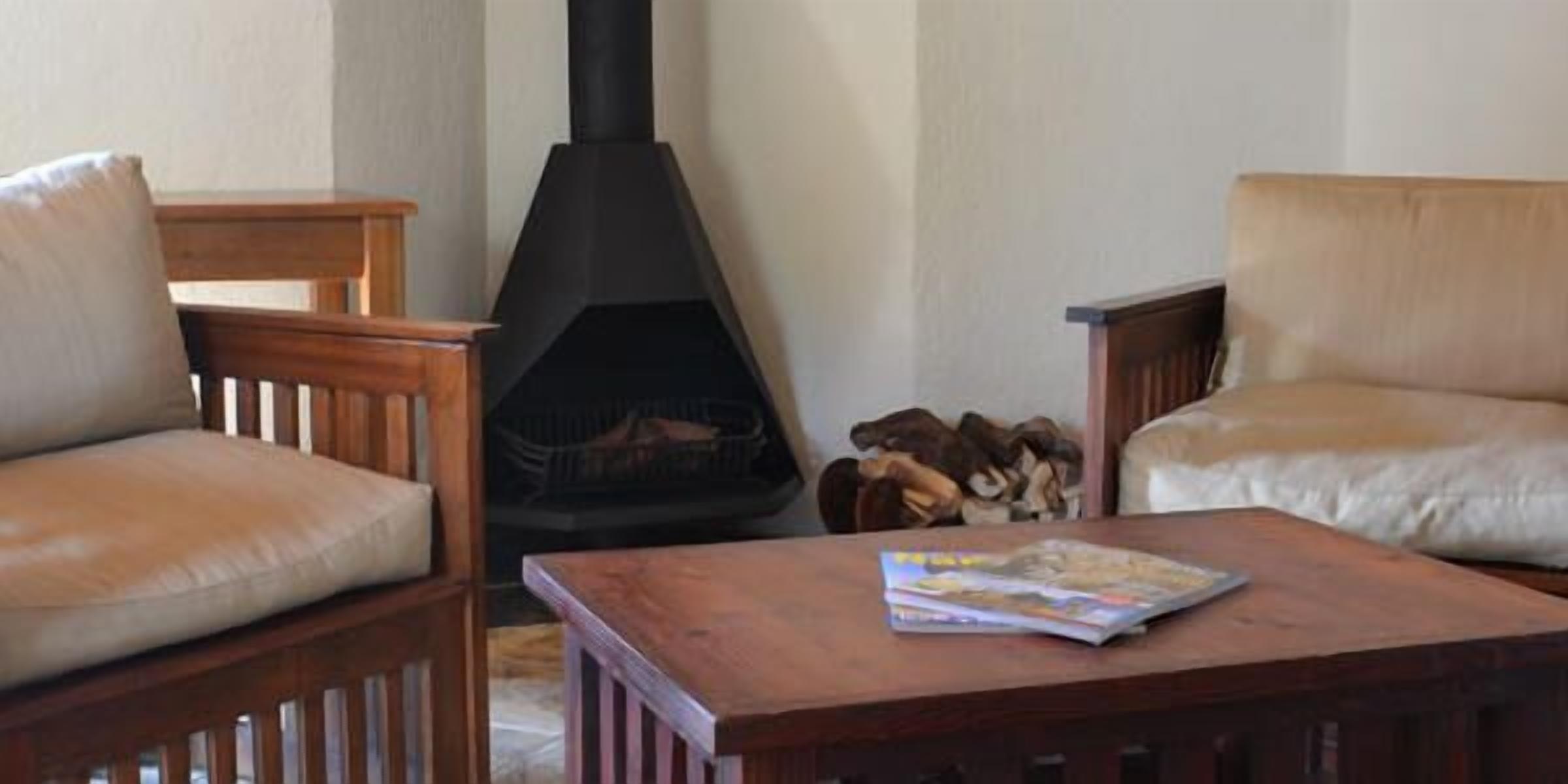 A cozy living room with two wooden chairs, a wooden coffee table, and a black wood-burning stove.