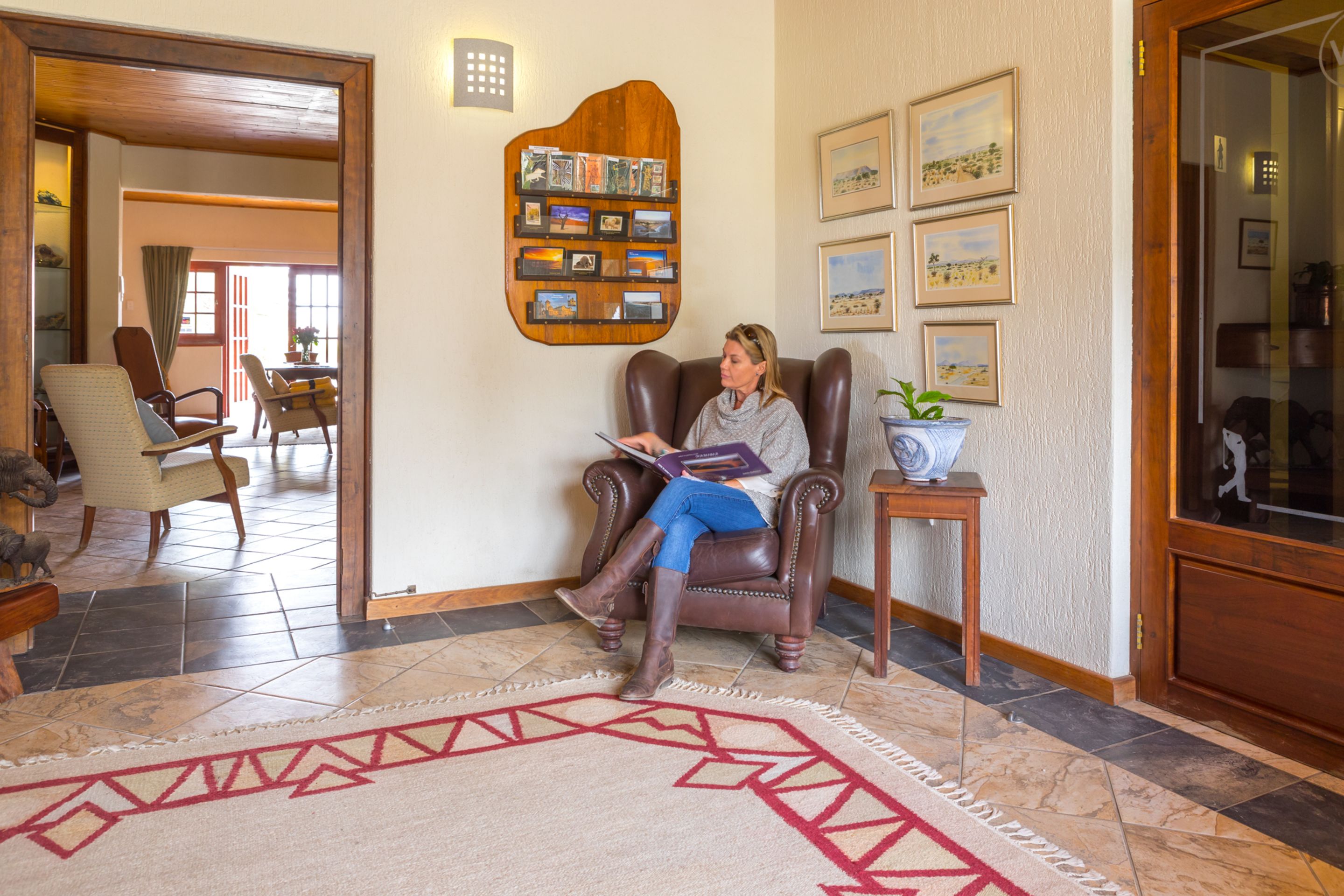 A person sitting in a leather armchair in a well-lit room with a patterned rug, a wooden shelf with photos, and framed pictures on the wall.