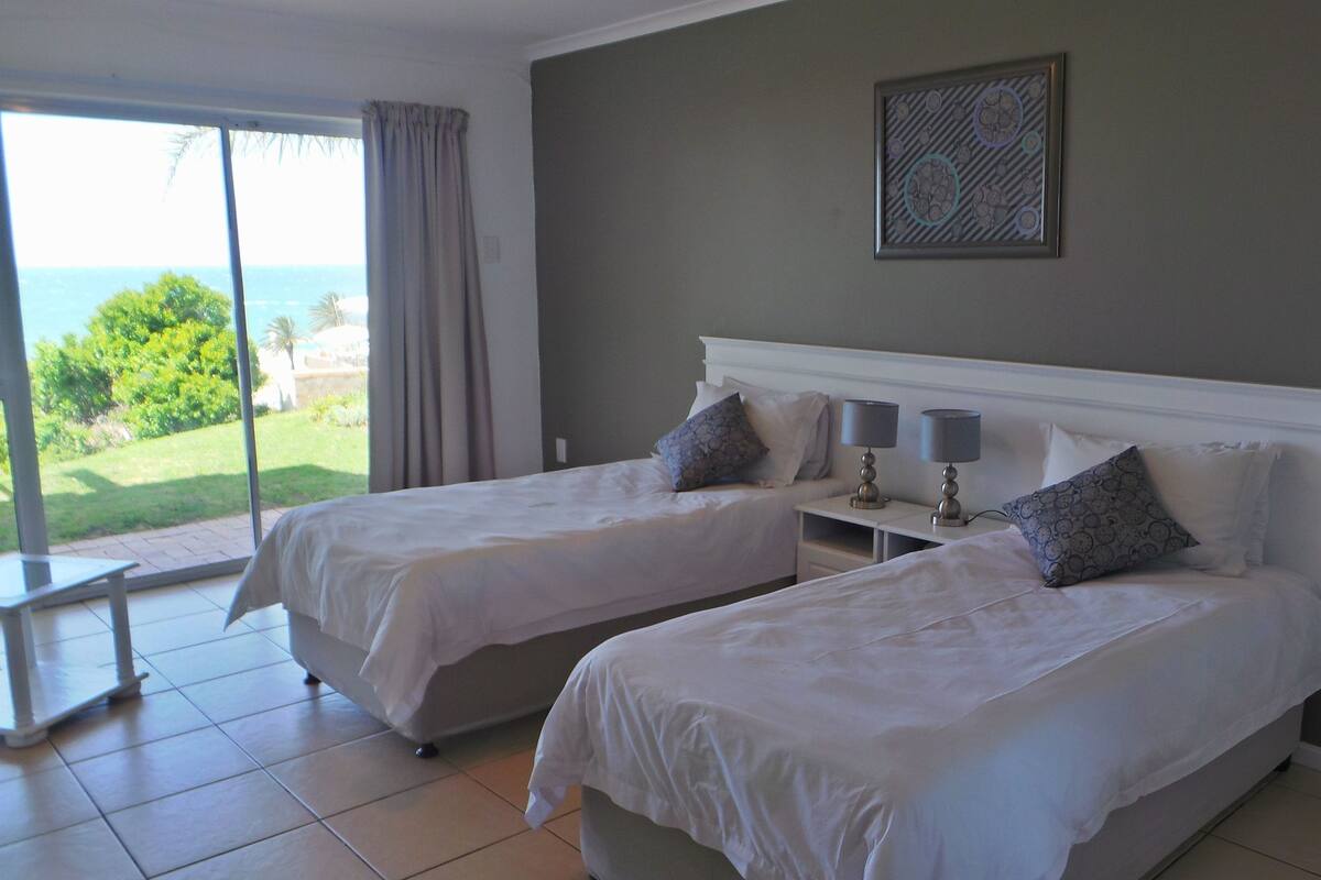 A hotel room with two beds, a view of the sea, and a framed artwork on the wall.