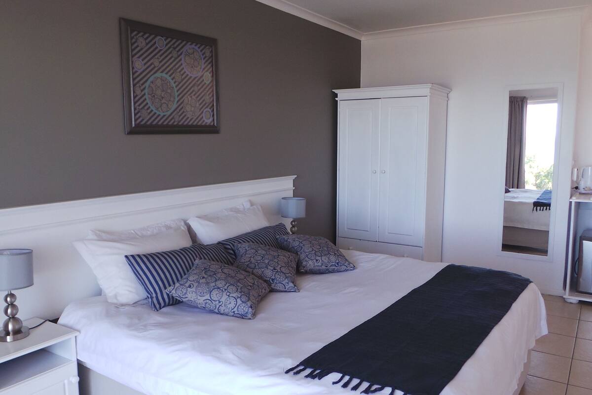 A neatly made bed with a white headboard, a bedside table with a lamp, a wardrobe, and a view of the room's interior.