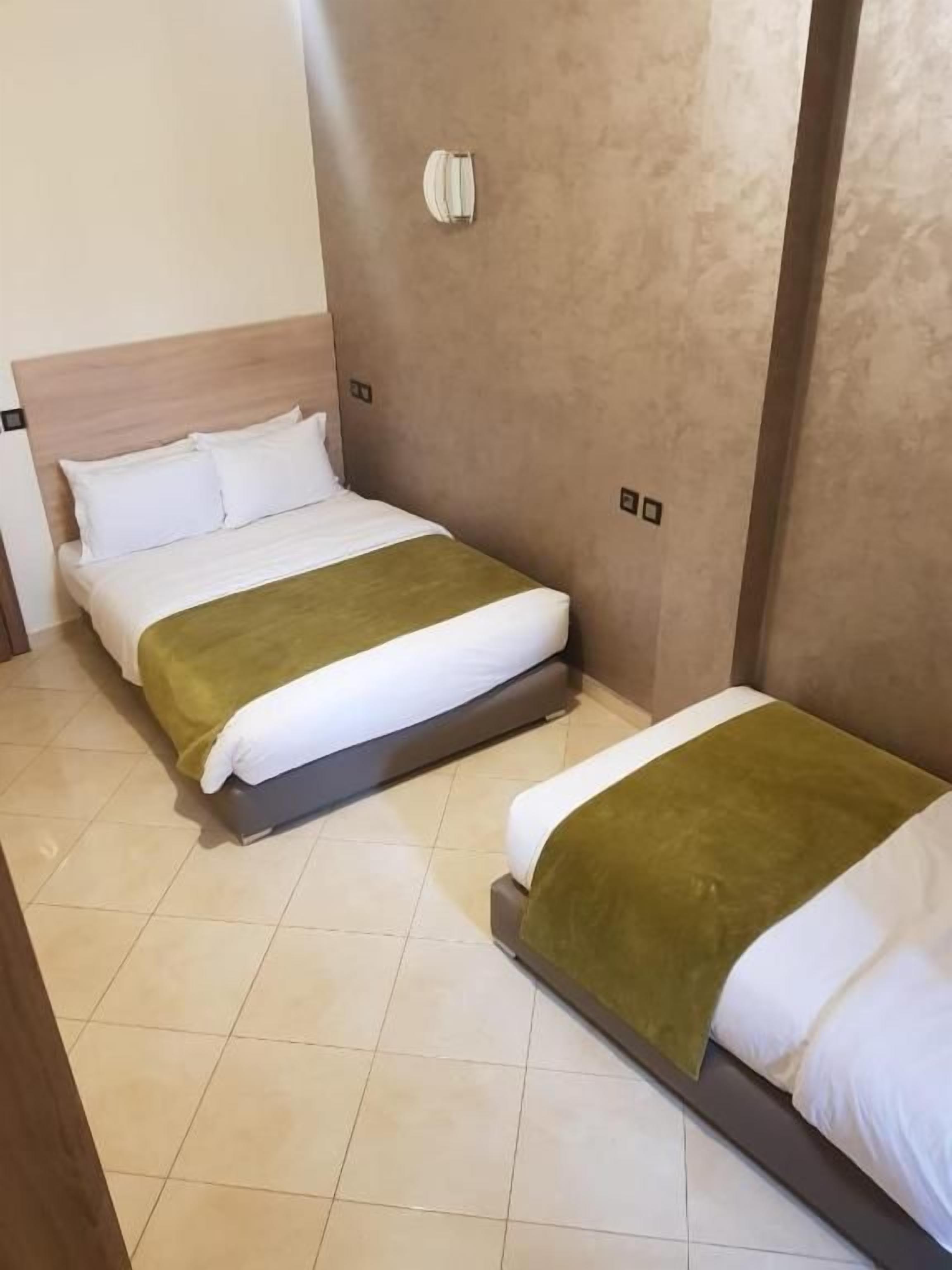 Una habitación de hotel con dos camas, cada una con colcha verde y blanca, y cabeceros de madera.