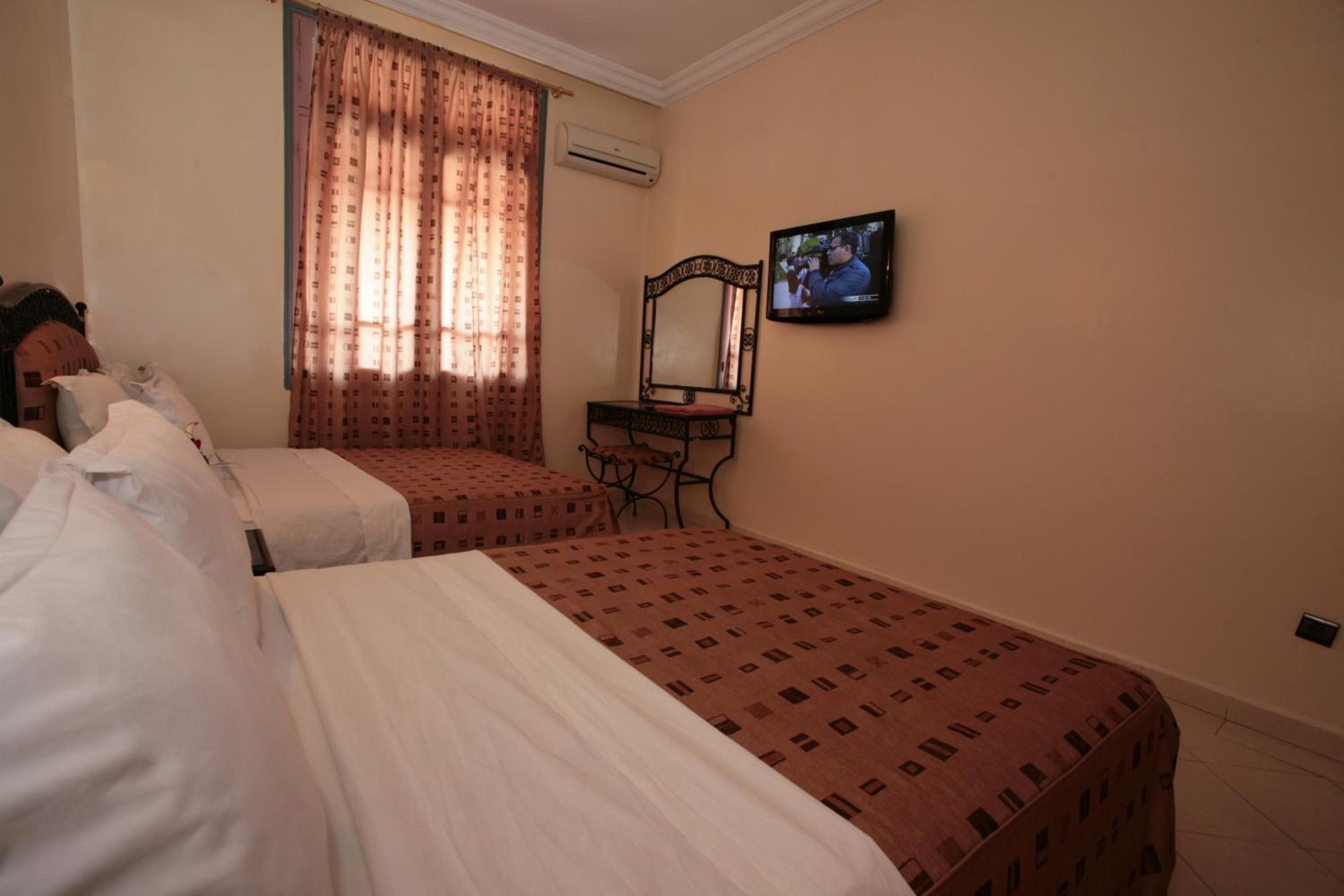Une chambre d’hôtel avec deux lits, une télévision, un appareil de climatisation et une fenêtre avec des rideaux.