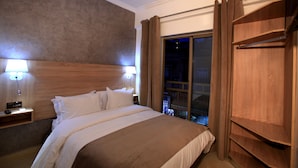 A hotel room with a large bed, two bedside lamps, a wooden headboard, a window with curtains, and a wooden wardrobe. - Hôtel Ichbilia (Marrakech)