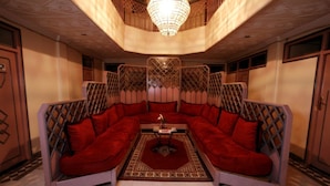 A spacious living room with a large L-shaped red sofa, a central coffee table, and a patterned rug. - Hôtel Ichbilia (Marrakech)