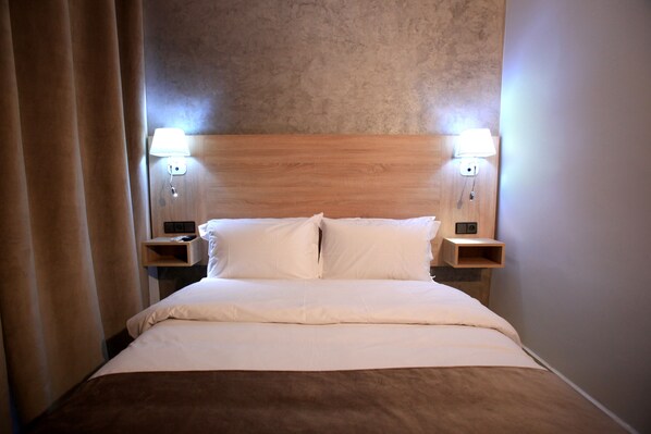 Un lit bien fait, avec du linge de lit blanc, deux tables de chevet avec des lampes et une tête de lit en bois.