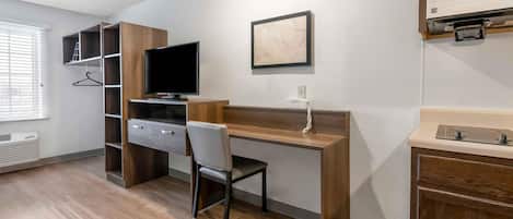 Quarto de hotel compacto com escrivaninha de madeira, uma cadeira, televisão, quadro emoldurado, micro-ondas embutido e um pequeno banheiro.