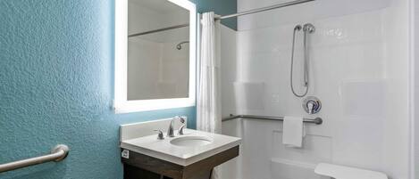 A bathroom with a white sink, a mirror, a shower with a handheld showerhead, and a towel rack.