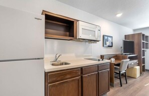 A compact kitchen with a built-in microwave, a sink, and wooden cabinets. - Extended Stay America Select Suites - Clearwater (Clearwater)