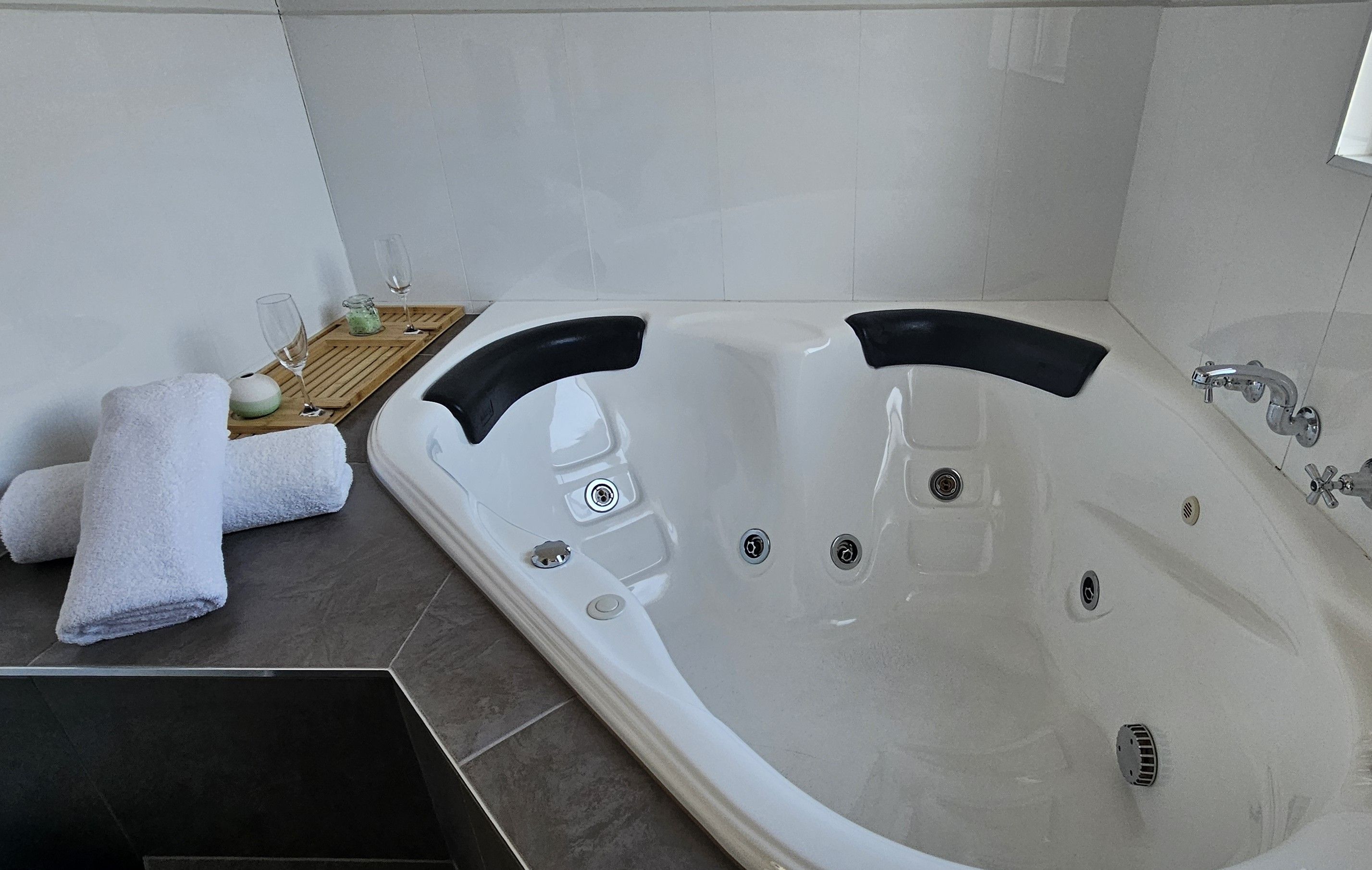 Un baño moderno con una bañera grande, una bandeja de madera con artículos de aseo y un juego de toallas.