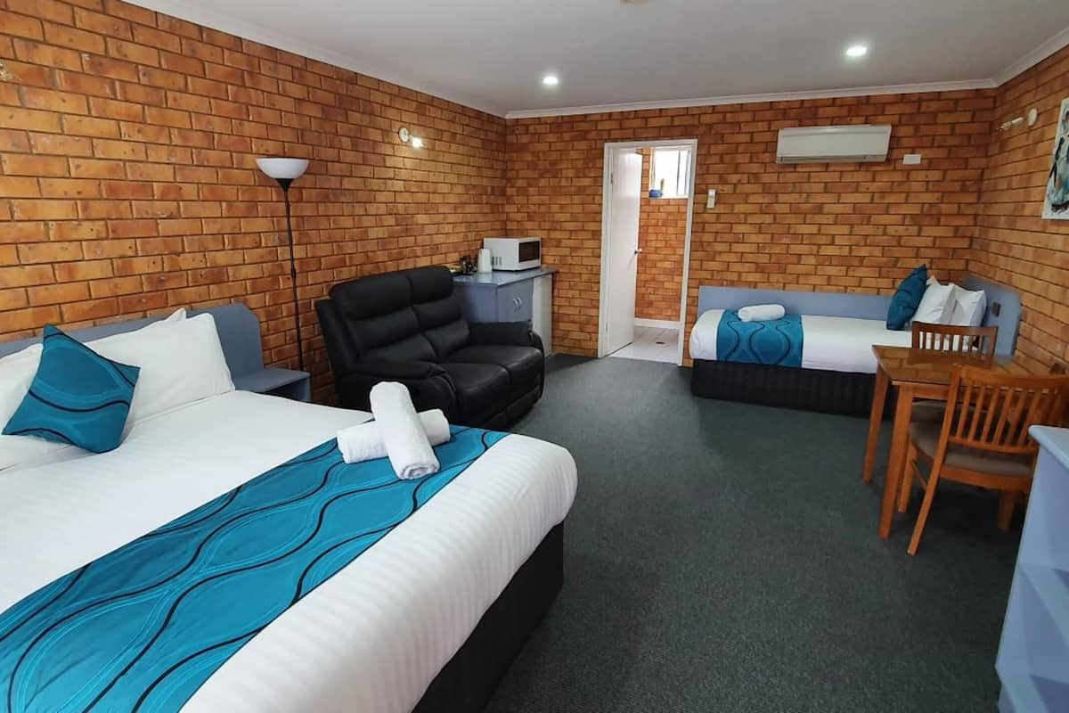 A hotel room with a brick wall, two beds, a desk, a chair, and a door leading to another room.