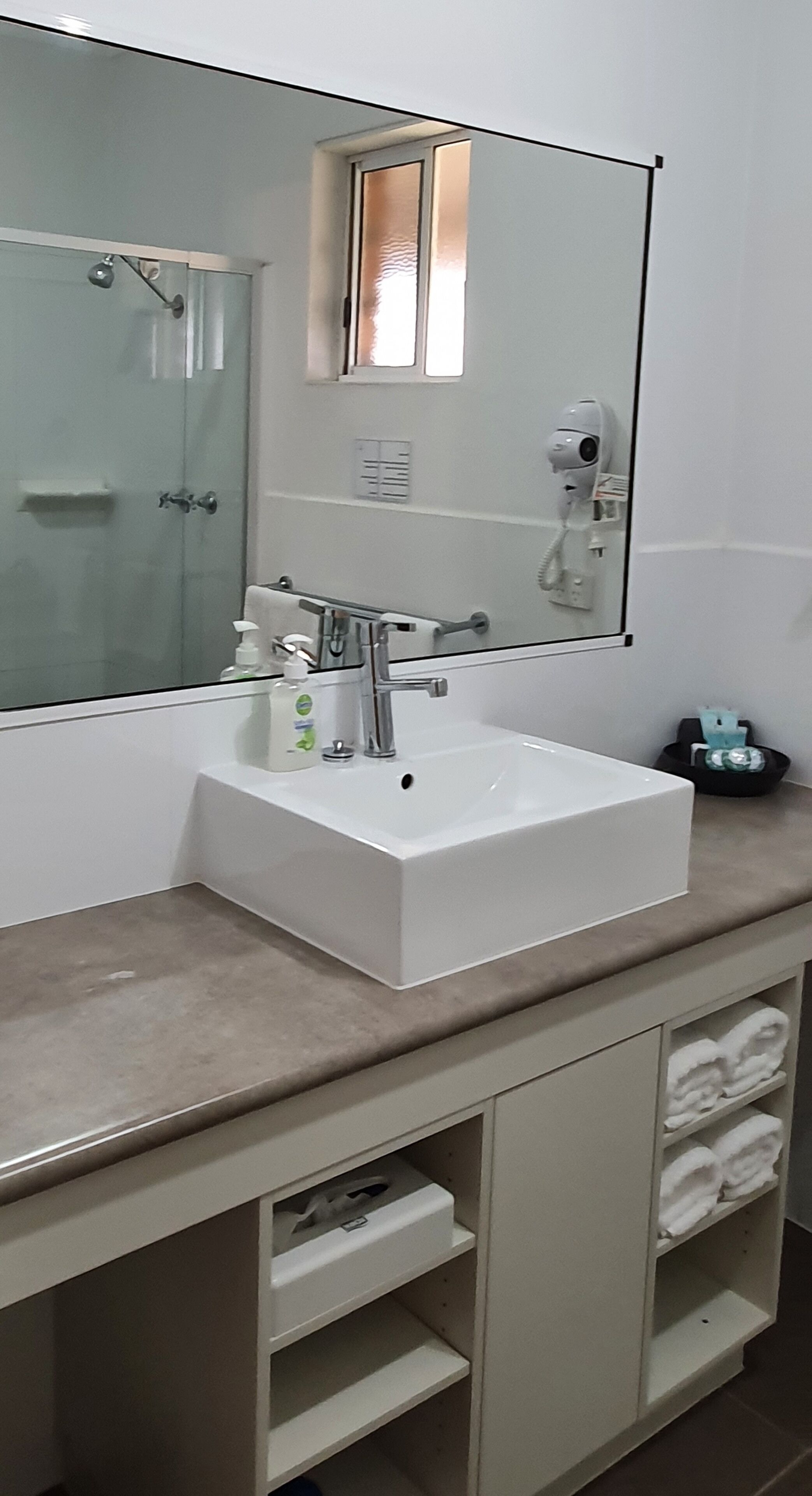 Une salle de bain moderne avec un grand miroir, un lavabo blanc et une douche à parois de verre.