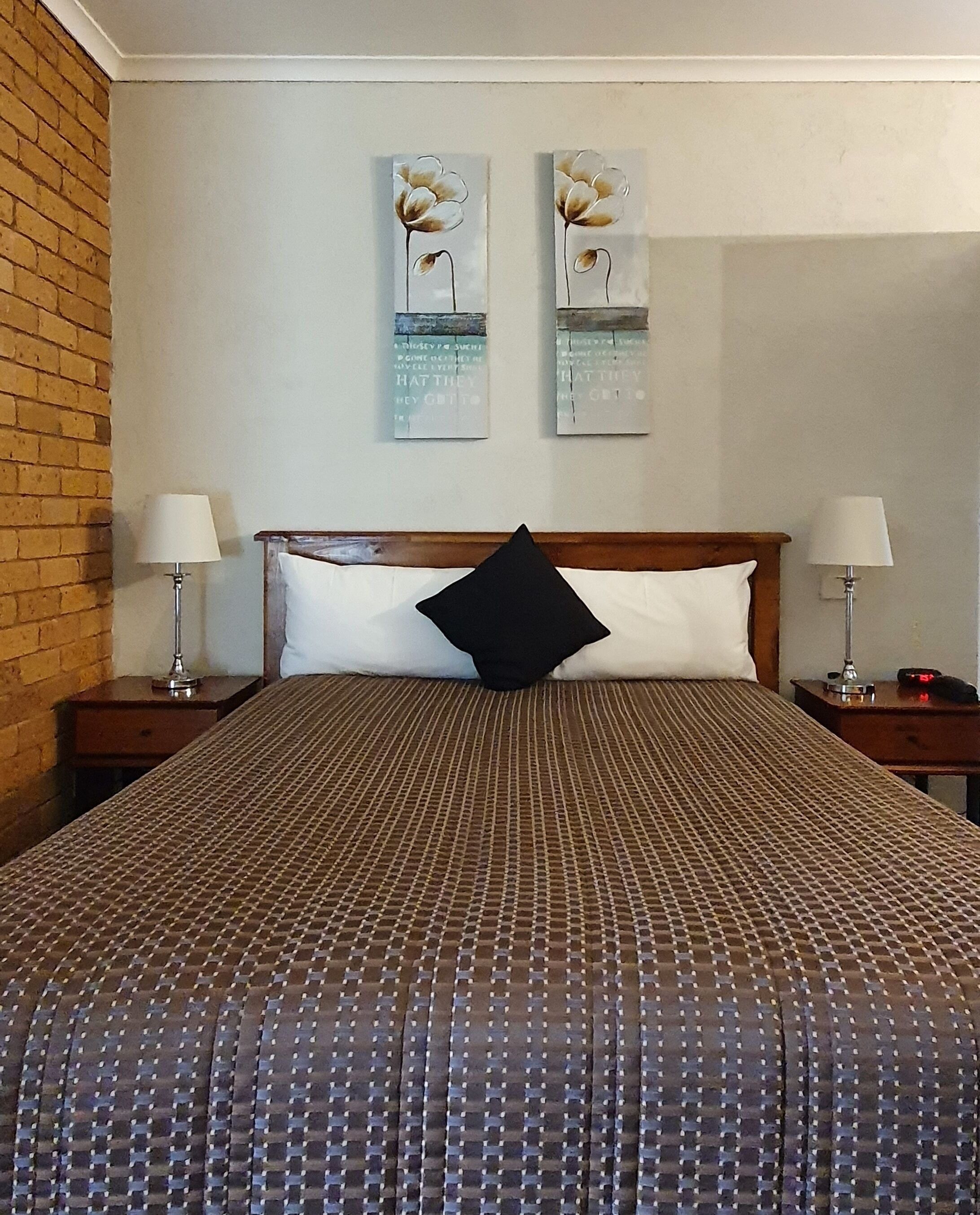 Ein Hotelzimmer mit einem großen Bett, zwei Nachttischen, einem schwarzen Kissen und zwei an der Wand befestigten Bildern.