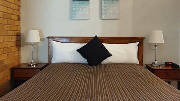 Ein Hotelzimmer mit einem großen Bett, zwei Nachttischen, einem schwarzen Kissen und zwei an der Wand befestigten Bildern.