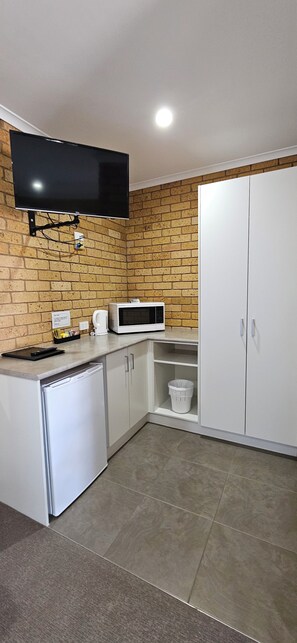 A compact kitchen with a flat-screen TV, a microwave, and a dishwasher. - Centrepoint Motel (Deniliquin)