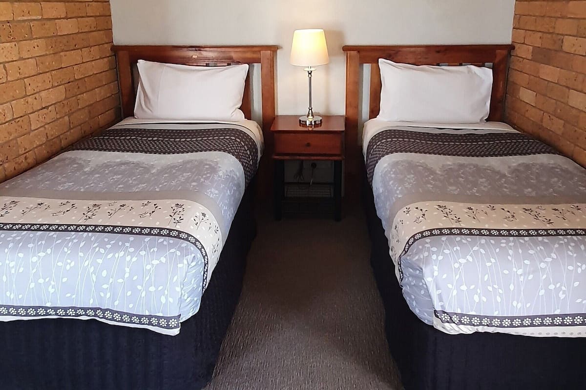 A hotel room with two beds, a nightstand with a lamp, a framed picture on the wall, and a carpeted floor.