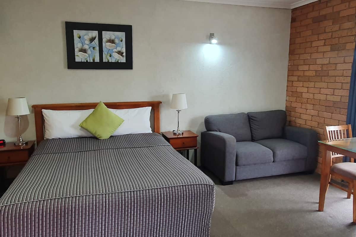 A hotel room with a bed, a grey sofa, a small table with chairs, a lamp, and a picture on the wall.