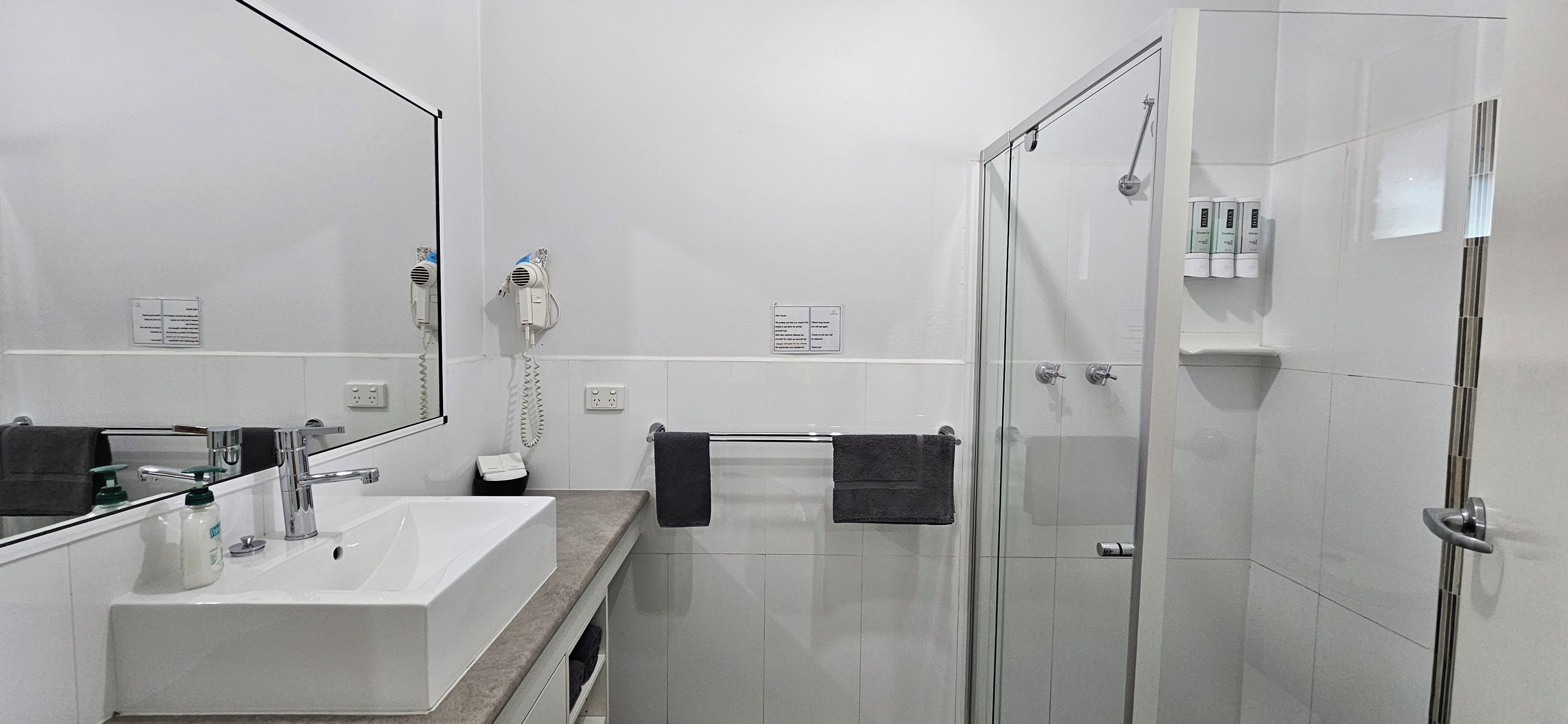 A modern bathroom with a white sink, a mirror, a hairdryer, and a glass shower enclosure.