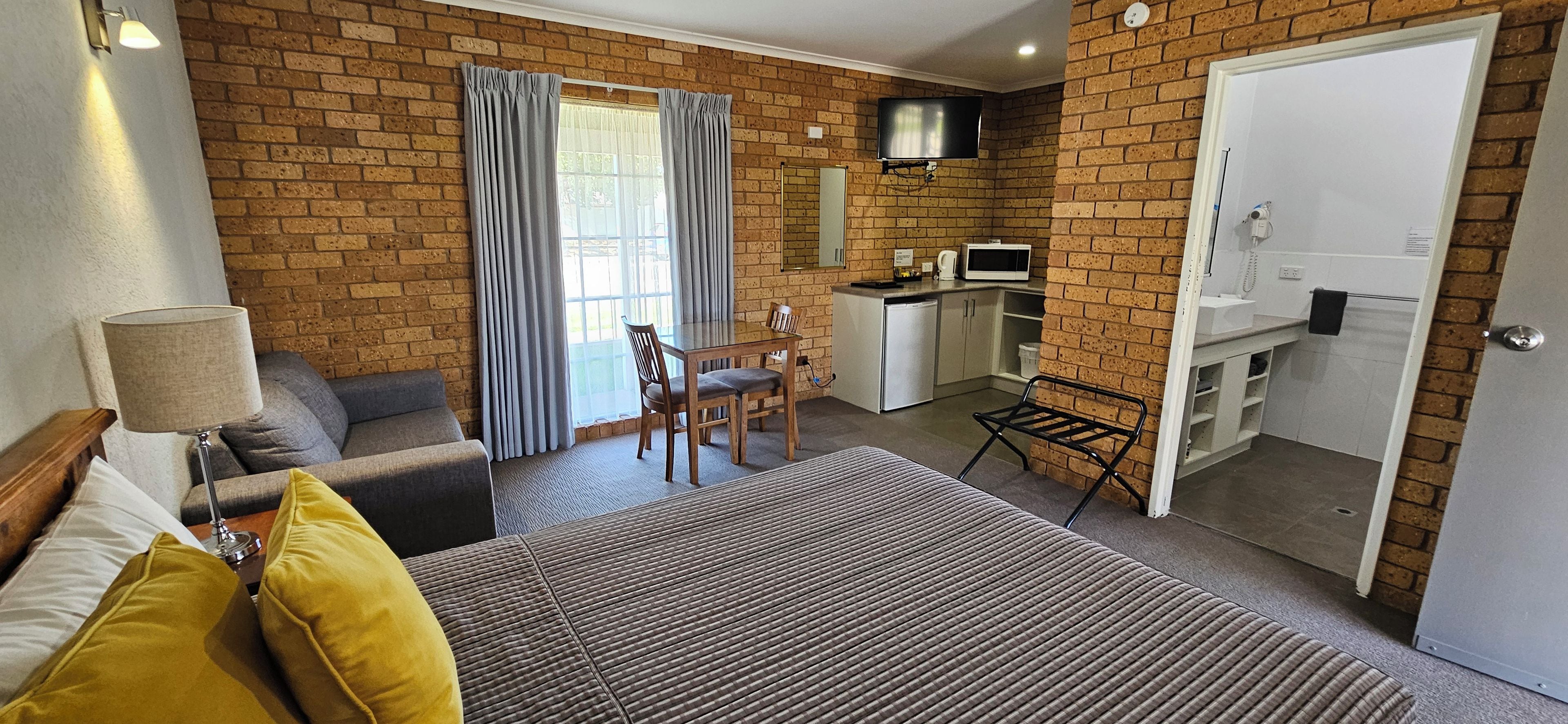 A room with a bed, a desk, a chair, a TV, and a kitchenette.