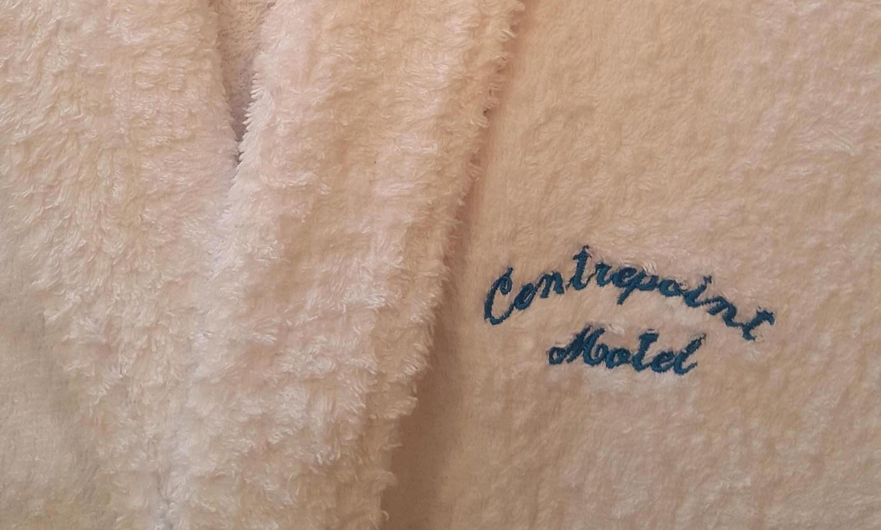 Close-up de tecido macio e texturizado com bordado que diz 'Contrevent Hotel'.