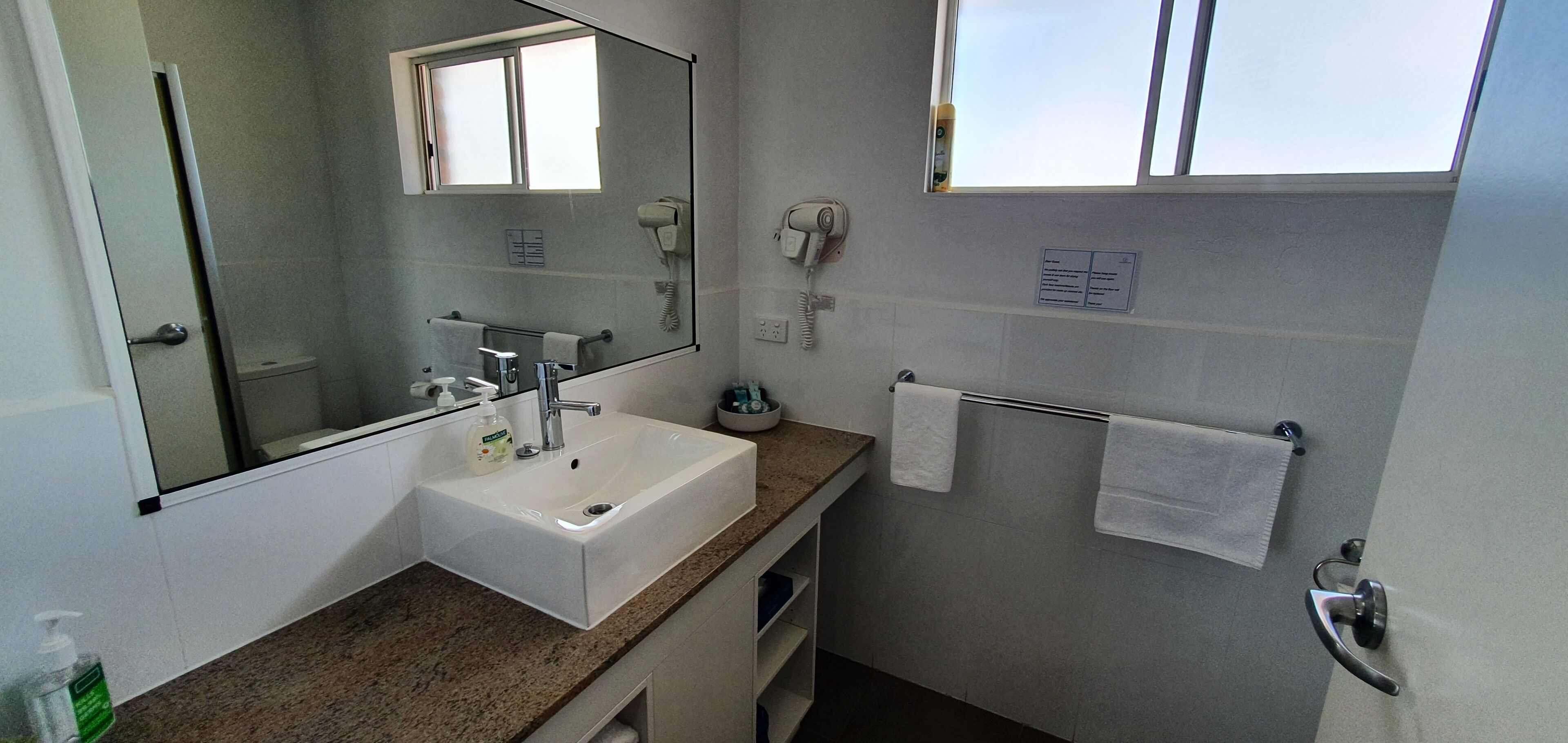 Een badkamer met een wastafel, spiegel, handdoekhouder en een haardroger.